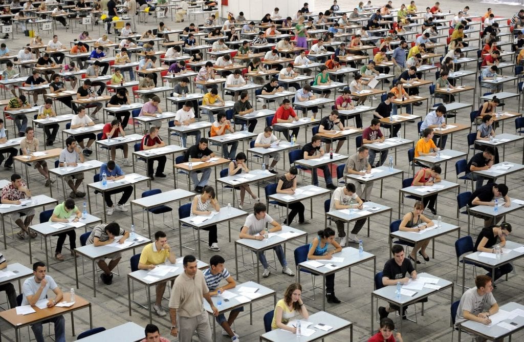 Large exam hall with hundreds of students at desks sitting an exam
